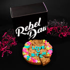 Cookie cake gift featuring a decorated chocolate chip cookie with colorful frosting, sprinkles, and bold blue lettering reading