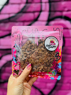 Gourmet oatmeal and chocolate lactation cookie in vibrant Rebel Daughter Cookies packaging, held against a pink graffiti wall.