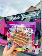 Cinnamon oatmeal and raisins white chocolate specialty cookies in vibrant packaging, held in front of a Rebel Daughter Cookies mural.