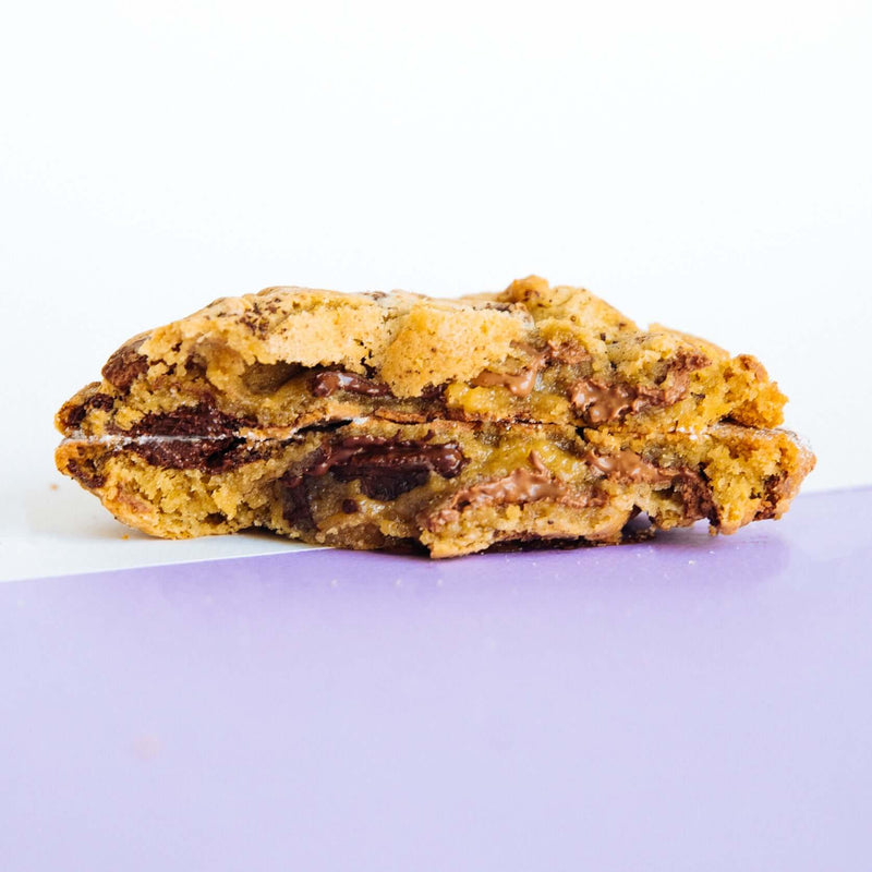A Rebel Daughter gourmet chocolate chunk "O(M)G" cookie in half and stacked against a purple background