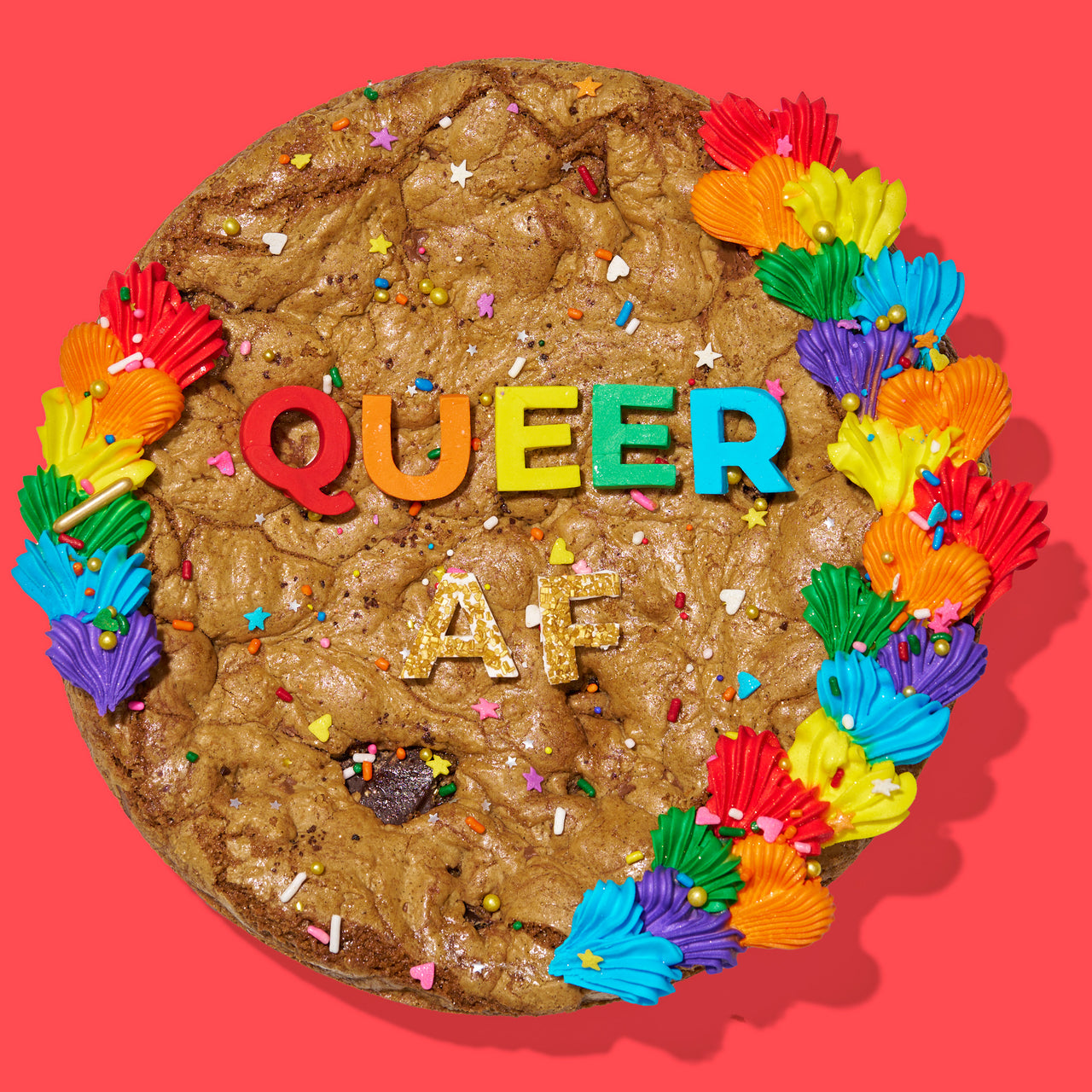 Decadent cookie cake decorated with rainbow frosting, sprinkles, and bold lettering that reads "QUEER AF" on a red background.