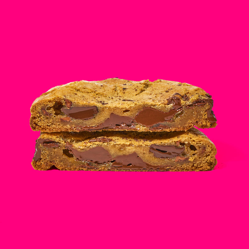 Decadent chocolate chip cookie with a gooey, melted chocolate center on a vibrant pink background.