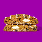 Oatmeal raisin decadent cookies with a gooey cream filling, drizzled with vanilla icing on a vibrant purple background.