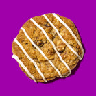 Oatmeal and raisins specialty cookie with a golden-brown texture, drizzled with vanilla icing on a bold purple background.