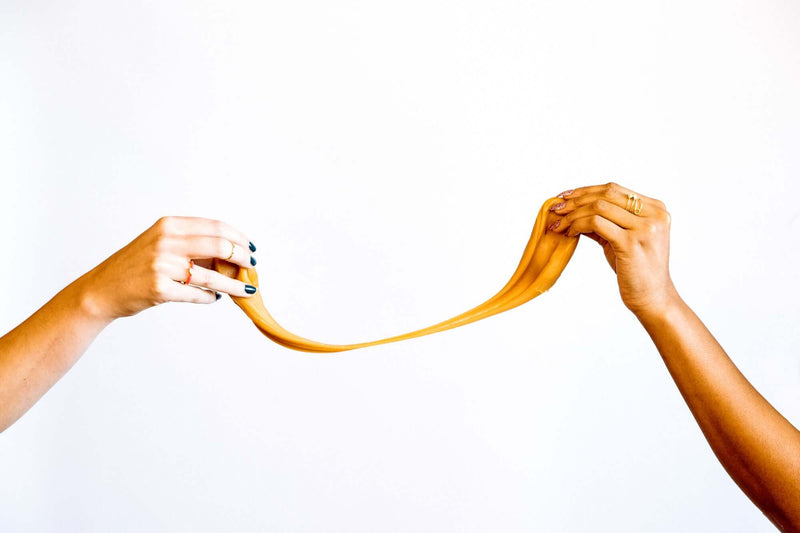 Two hands pulling a chunk of gooey caramel apart against a white background