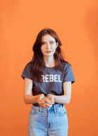 A gif of a girl in a REBEL shirt against an orange background throwing Fruity Pebbles into the air like confetti