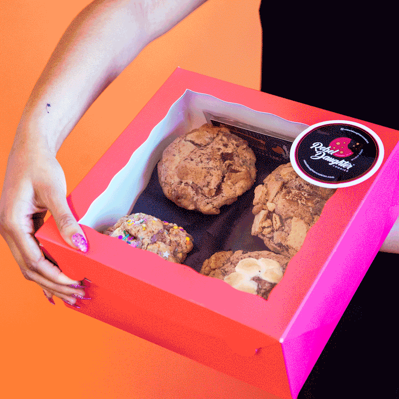 A gif of a woman's hand opening the lid on a pink Rebel Daughter Cookies delivery box with 4 cookies inside