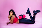 A woman lying on her stomach against a pink background with a pink Rebel Daughter Cookies delivery box balanced on her backside