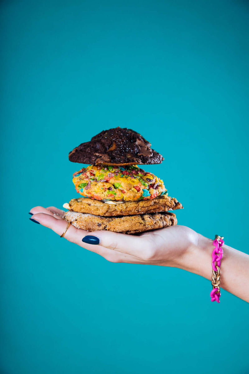 A woman's hand holding a stack of Rebel Daughter cookies against a turquoise background