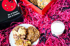 A Rebel Daughter Cookies lactation cookie sampler on a plate with a shipping box and milk surrounded by pink crinkle paper