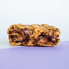 A gourmet chocolate chunk walnut Rebel Daughter cookie cut in half and stacked against a purple and white background