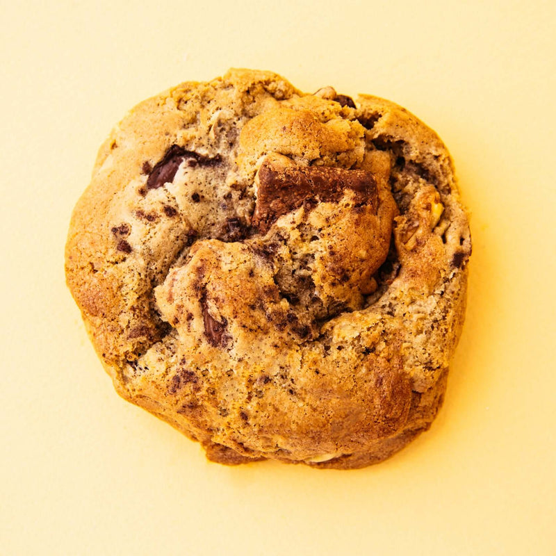 A gourmet chocolate chunk walnut Rebel Daughter cookie against a yellow background