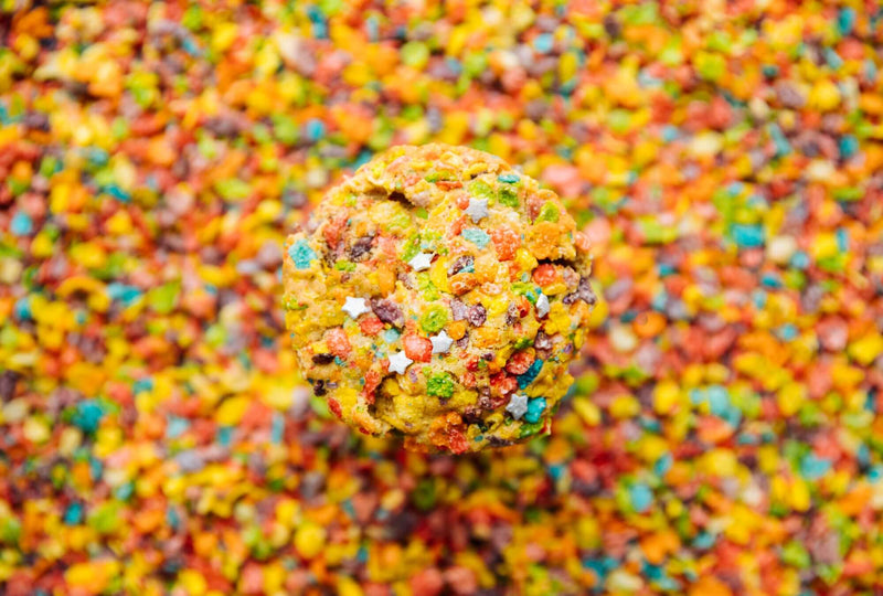 A colorful, gourmet Rebel Daughter White Unicorn cookie covered in Fruity Pebbles surrounded by Fruity Pebbles