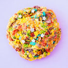 A colorful, gourmet Rebel Daughter White Unicorn cookie covered in Fruity Pebbles against a purple background