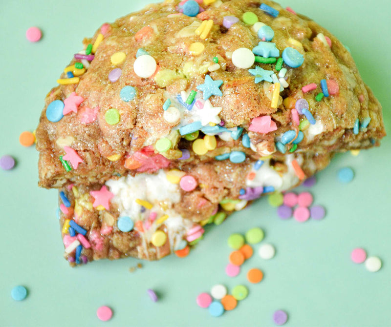 A Rebel Daughter Cookies Birthday Suit oatmeal lactation cookie in half with sprinkles on a turquoise background