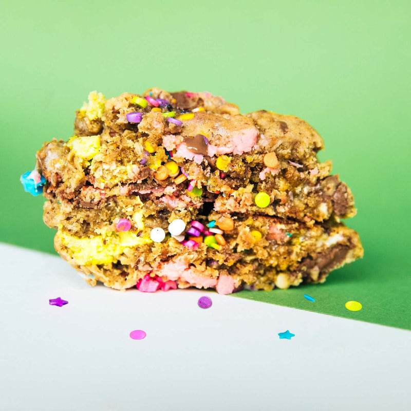 A Rebel Daughter Cookies Birthday Suit oatmeal lactation cookie in half with sprinkles on a green and white background