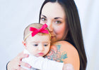 A woman with a shoulder tattoo holding her baby daughter wearing a pink bow